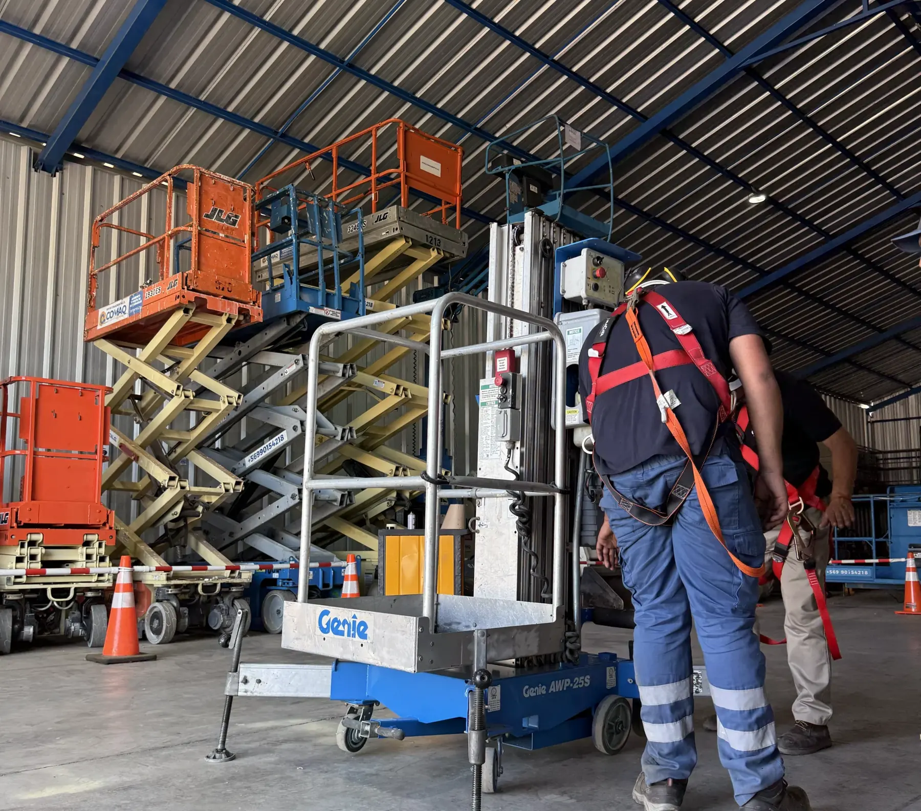 Dos técnicos revisando un elevador de personas dentro del galpón.