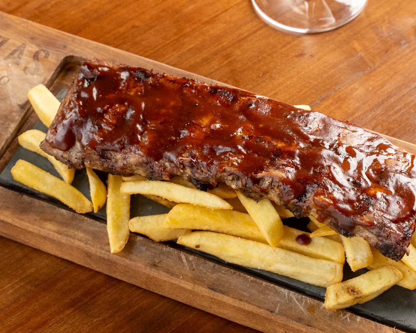 Costillas glaseadas sobre una tabla de madera, con papas fritas.