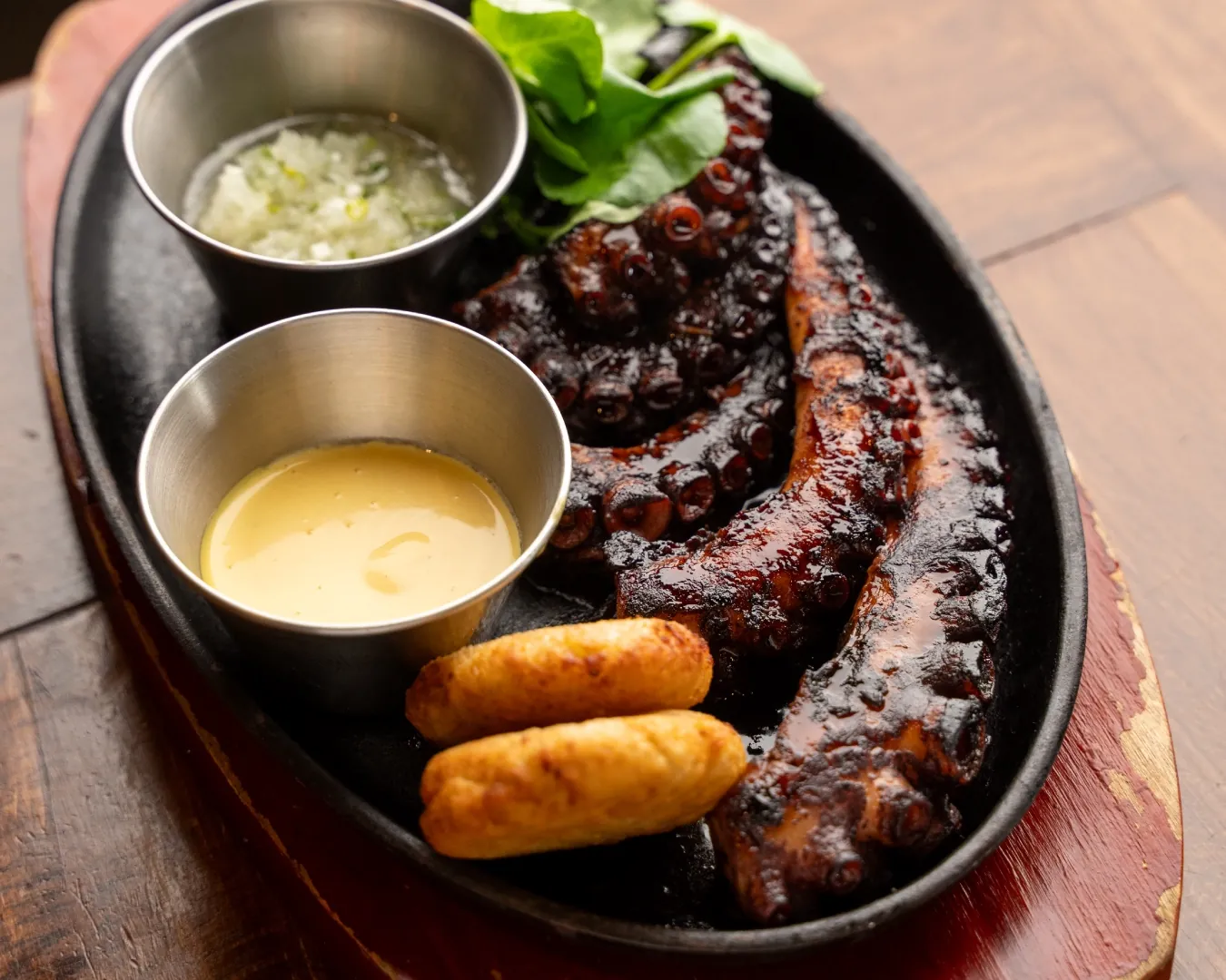 Pulpo a la parrilla con dos salsas y chapaleles, sobre una fuente de fierro.