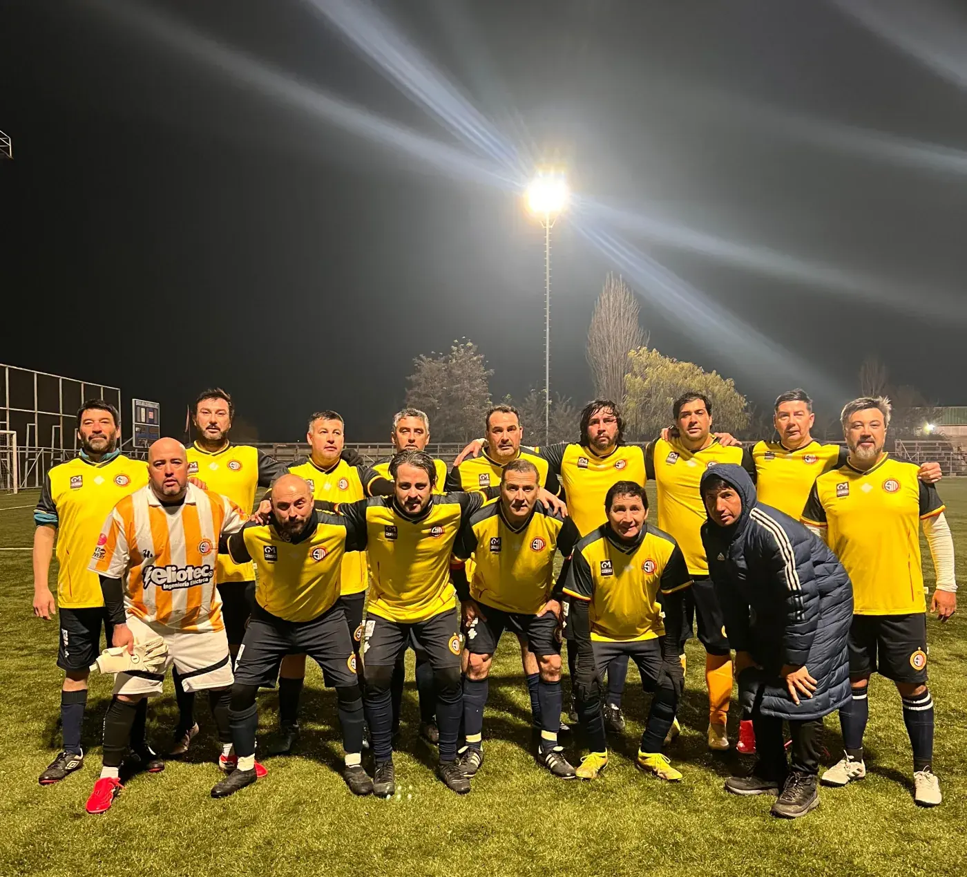 Plantel reunido en la cancha bajo los focos, de noche.